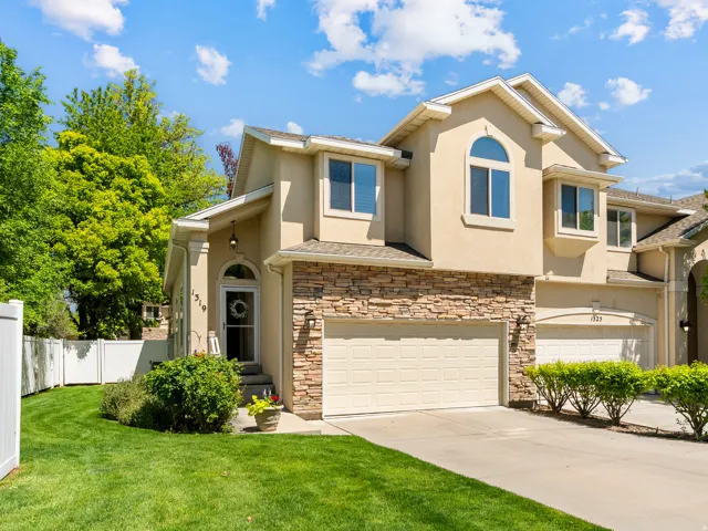 Stucco and stone facade home featuring an arched entryway, gabled rooflines, a two-car garage, and a manicured lawn