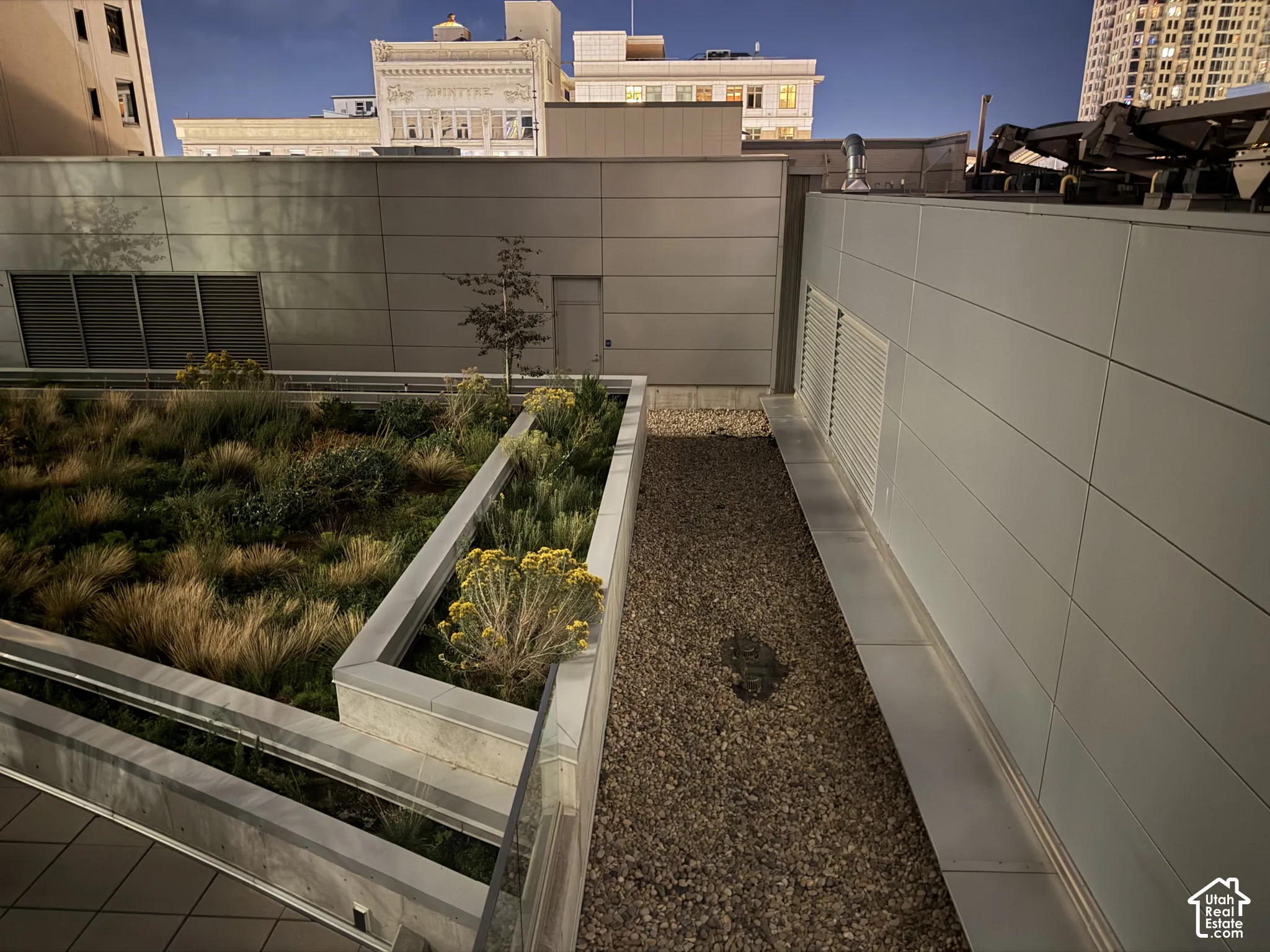 Rooftop green space featuring structured planters, varied vegetation, and a gravel pathway