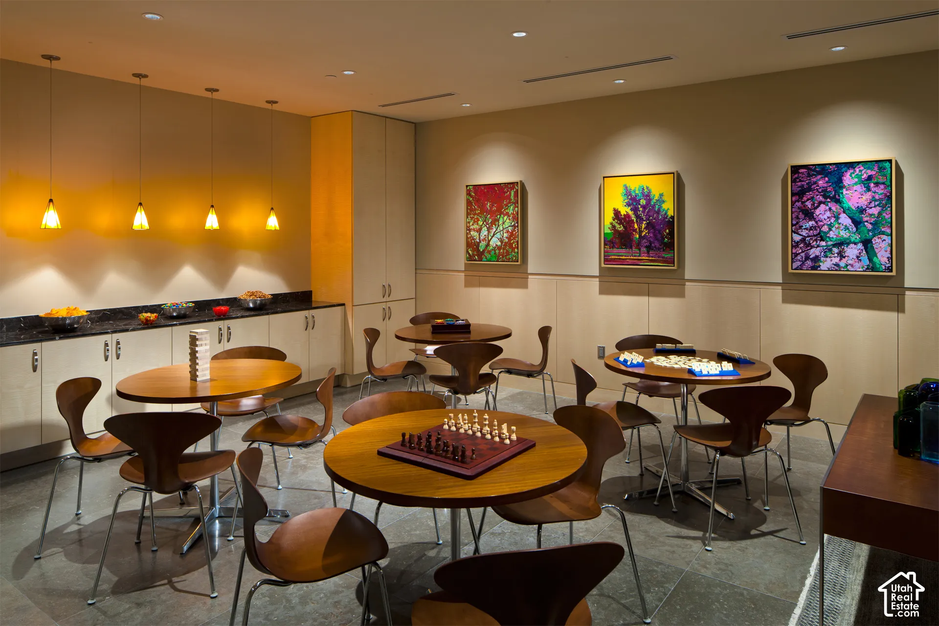 Recreational space featuring multiple round wooden tables, sleek chairs, stone flooring, and contemporary wall art