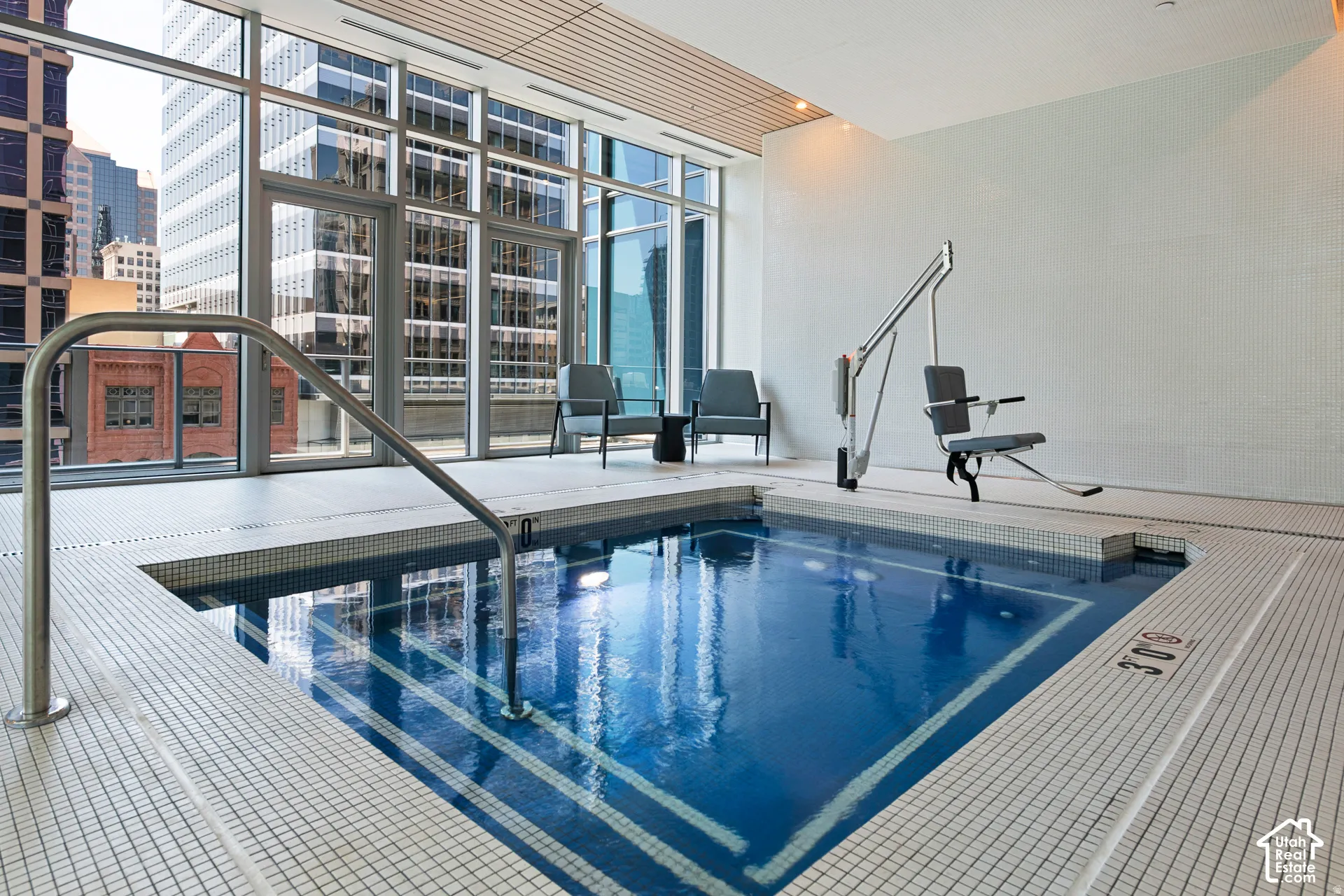 Indoor pool featuring a stainless steel grab bar, grid tile surround, and a mobility lift