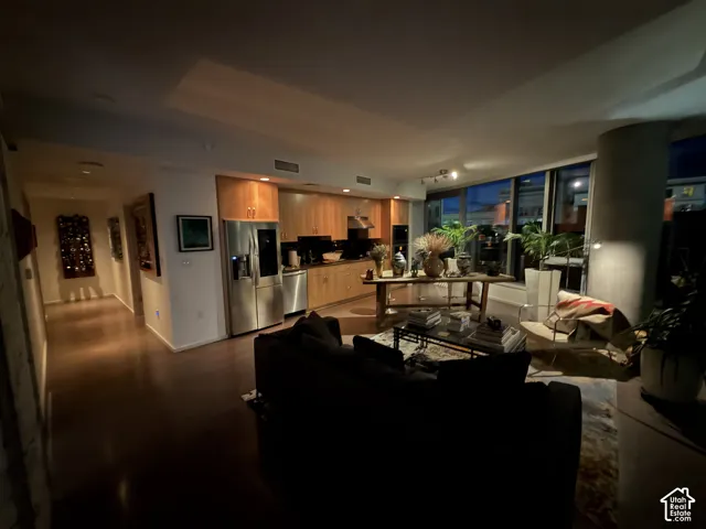 Open-concept living area featuring wood-finish flooring, a kitchen with stainless steel appliances and wood cabinetry, and expansive windows