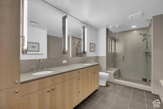Full bathroom featuring double vanity, dark tile patterned floors, a shower stall, and decorative backsplash