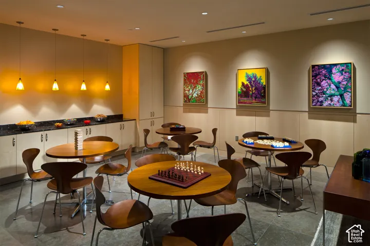Recreational space featuring multiple round wooden tables, sleek chairs, stone flooring, and contemporary wall art