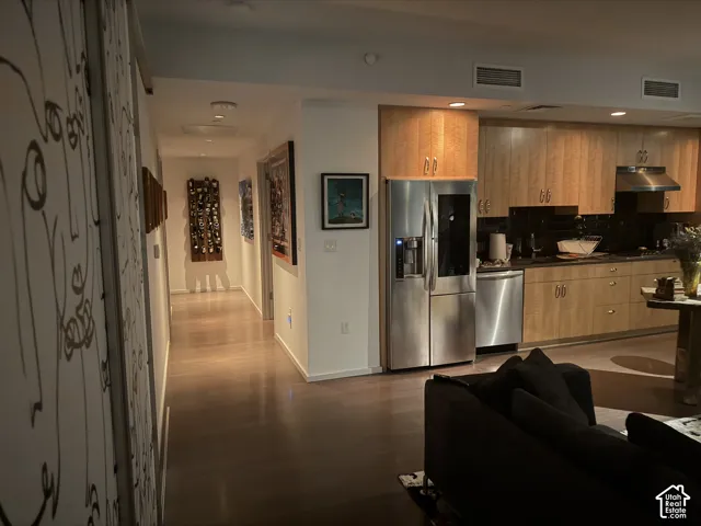 Kitchen featuring wood-finish cabinetry, stainless steel appliances, and a black subway tile backsplash