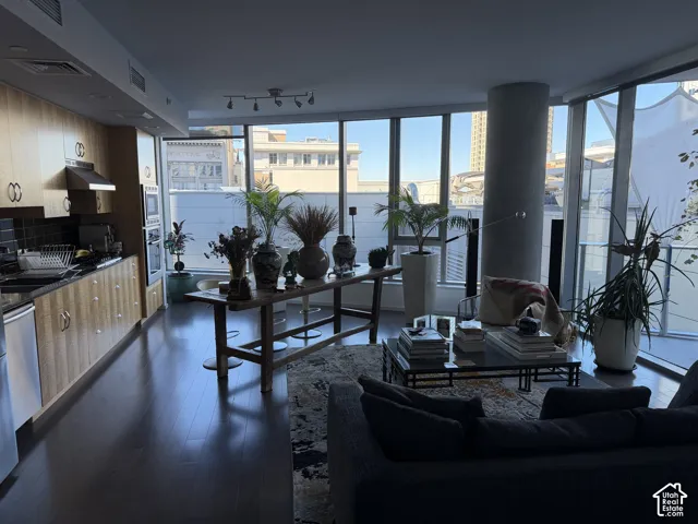 Expansive window walls, dark wood-finish flooring, a kitchen with integrated appliances, light wood cabinetry, and track lighting