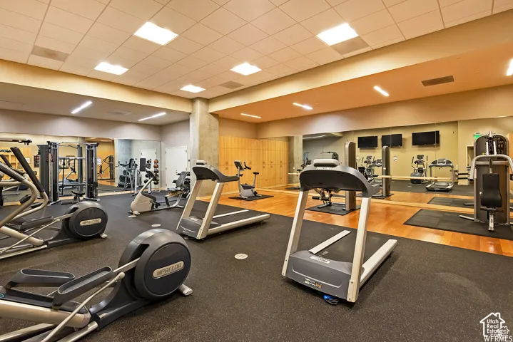 Fitness center featuring a rubberized flooring, mirrored wall, multiple cardio machines, strength training equipment, and wood-finish accent flooring