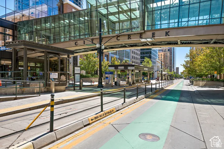 Urban street scene featuring light rail tracks, pedestrian walkways, and a covered station