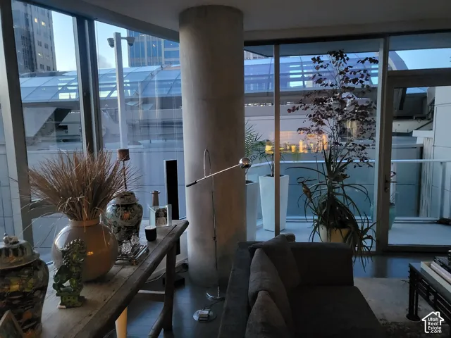 Floor-to-ceiling windows with expansive glass panels, concrete support pillar, dark wood-finish flooring, and a private balcony with glass railing