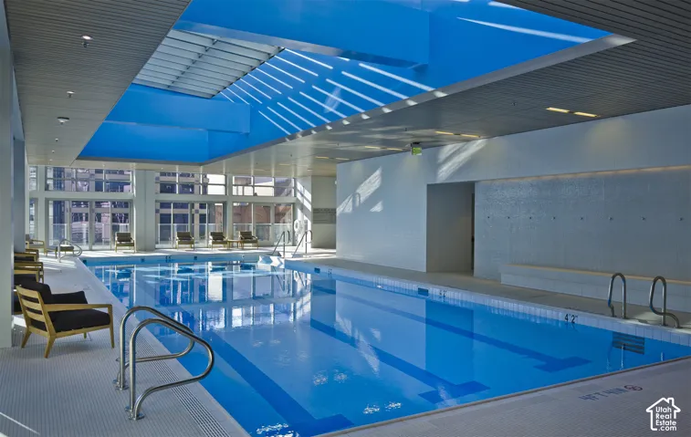 Indoor swimming pool featuring a large skylight, full-height windows, tiled deck, and built-in benches
