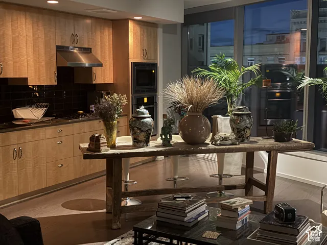 Kitchen featuring light wood-finish cabinetry, stainless steel appliances, dark subway tile backsplash, and wood-finish flooring