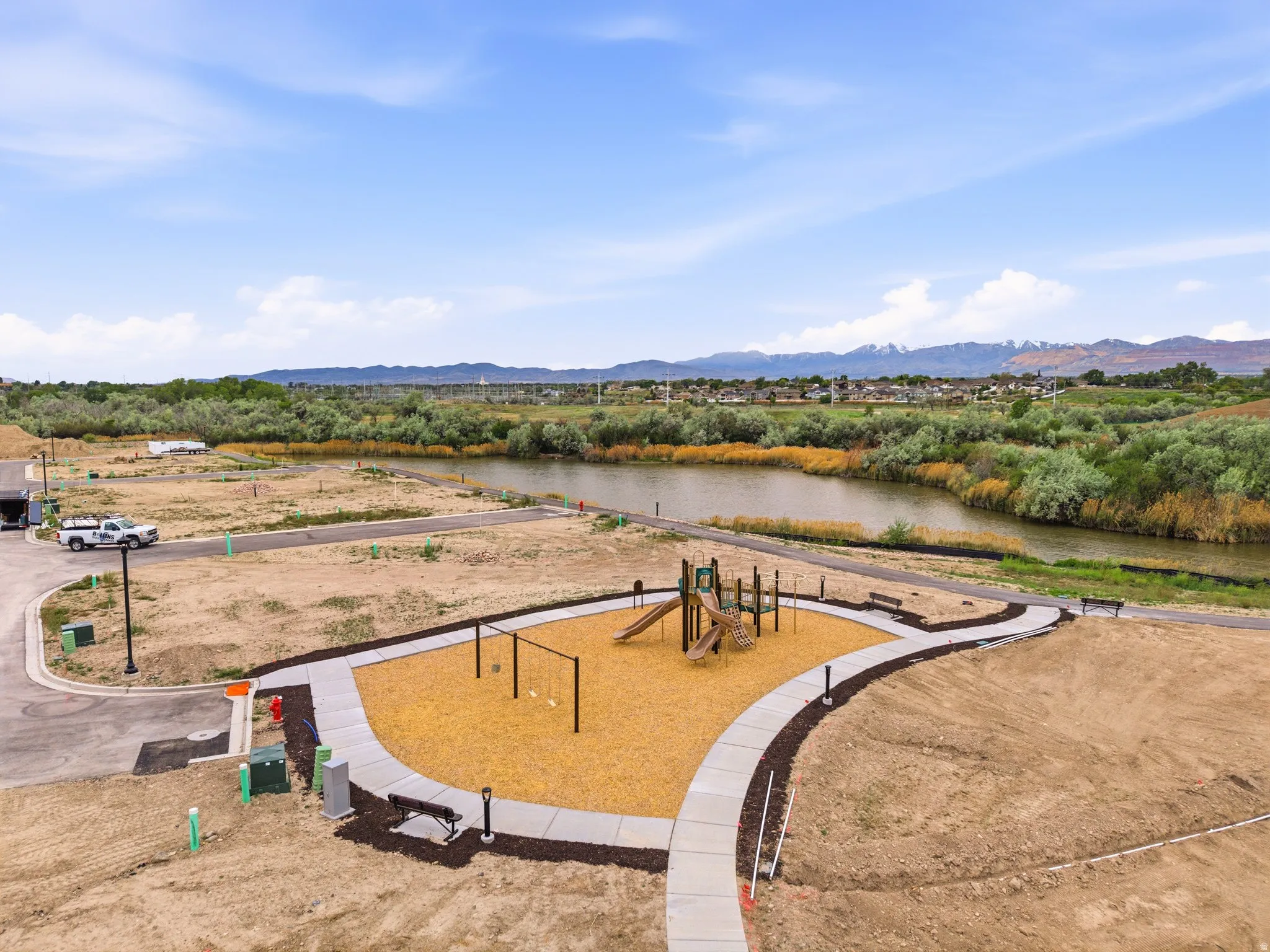 Community playground area featuring a play structure with slides and swings, a wood chip surface, and surrounding concrete pathways