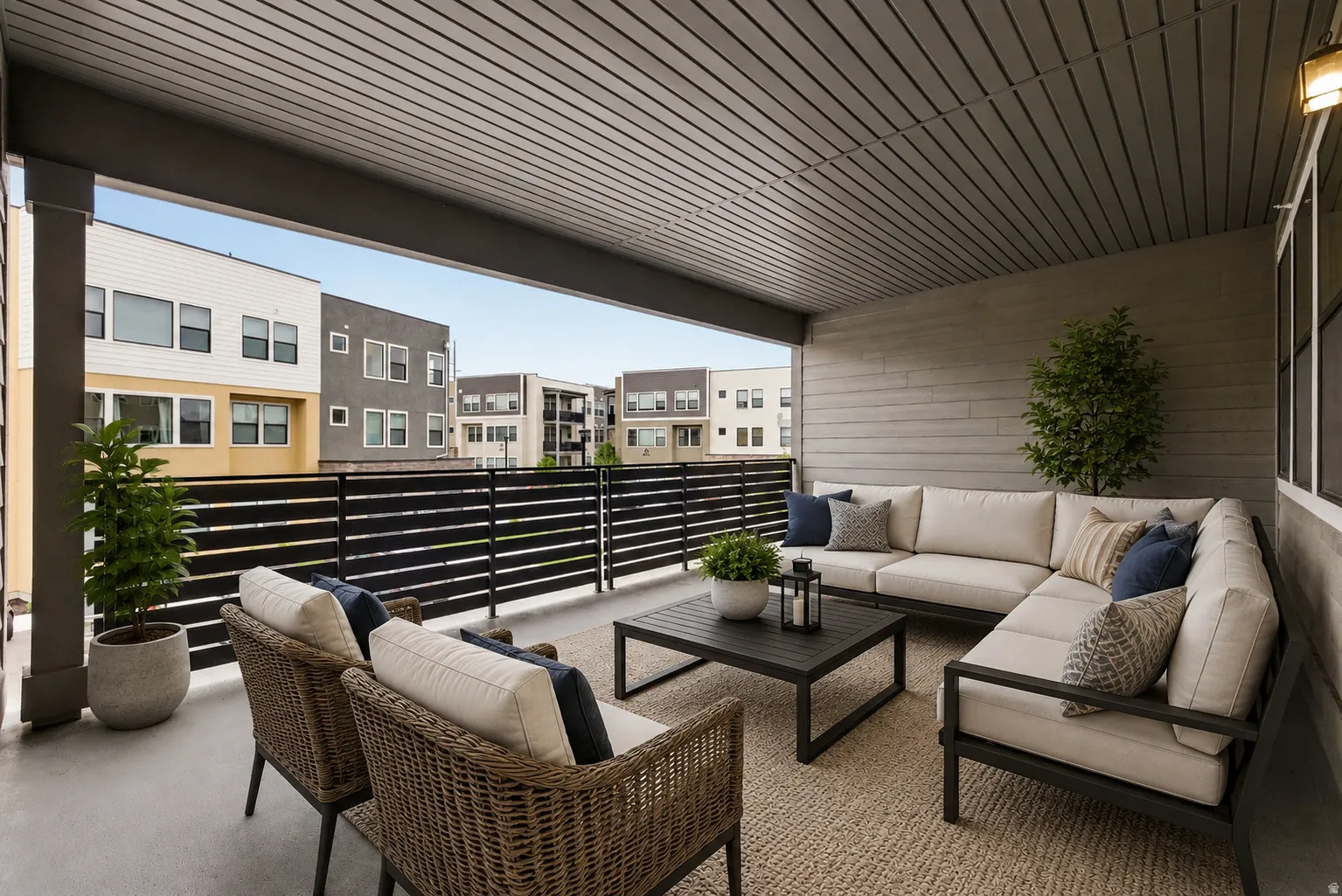 Covered outdoor patio featuring a slatted ceiling, horizontal plank siding, and a black slatted railing - Virtually Staged
