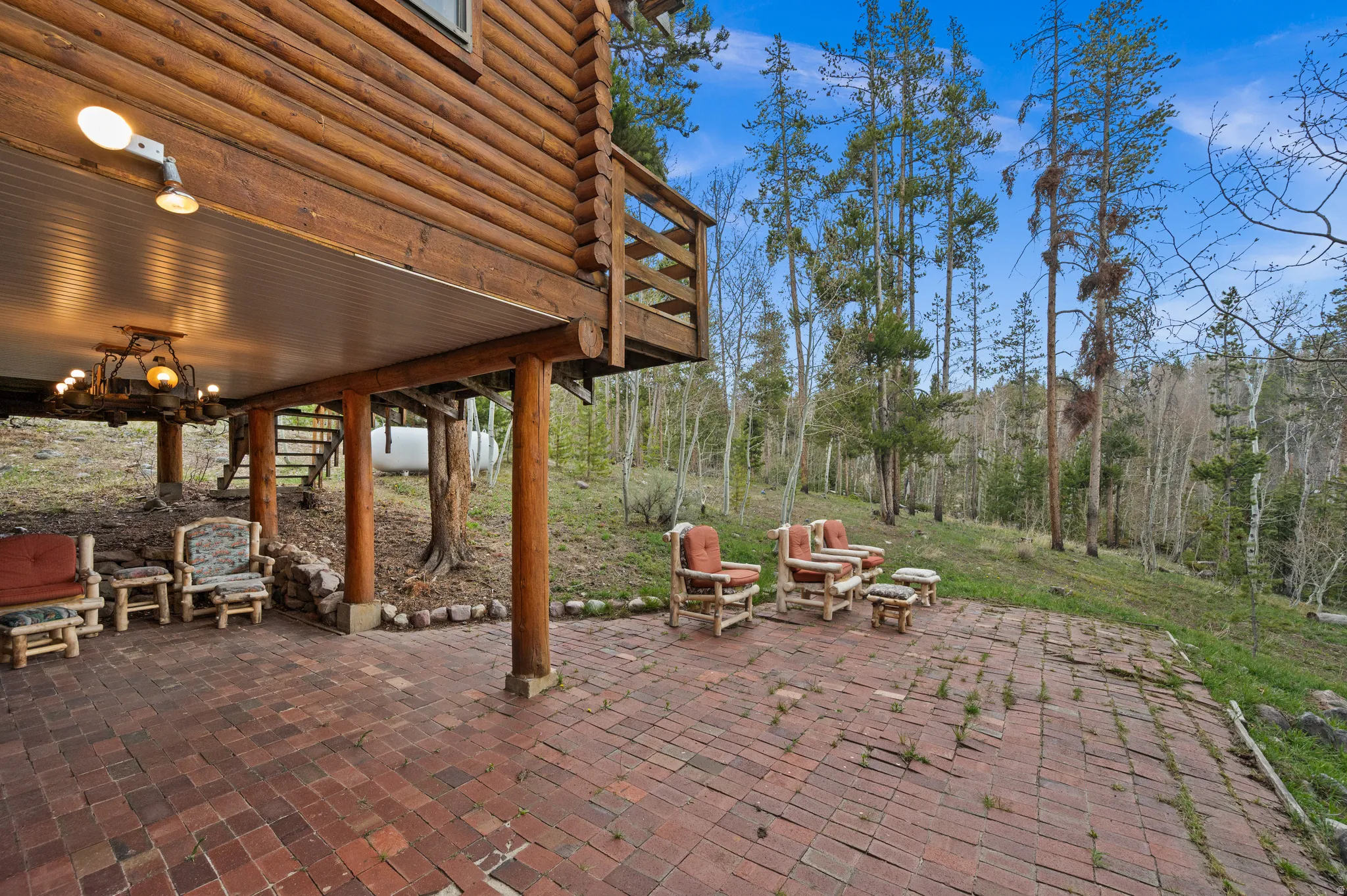 Expansive brick patio featuring a covered outdoor area with a rustic chandelier and a log cabin exterior