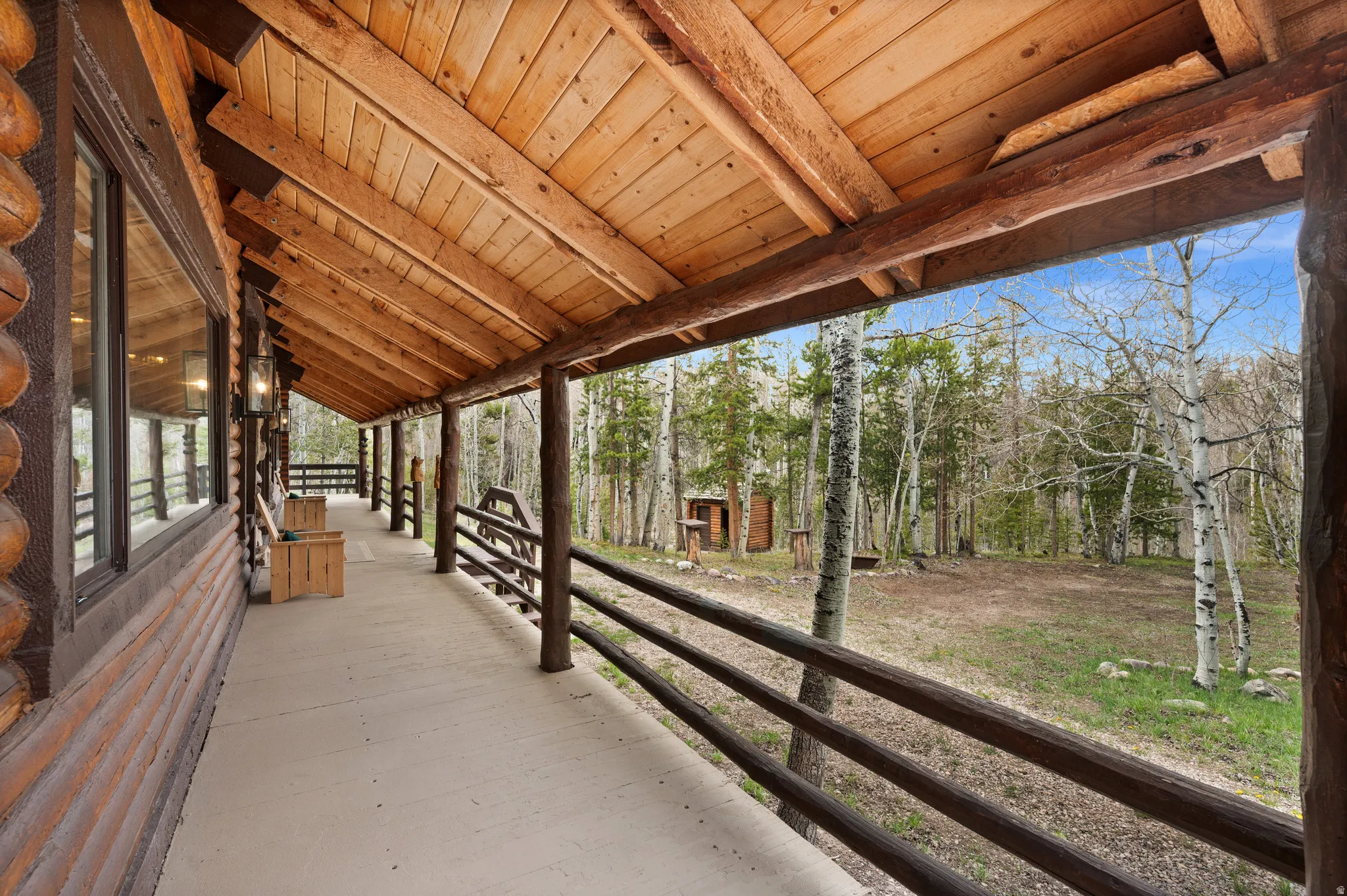 Expansive wrap-around porch featuring a log construction, exposed wood ceiling, rustic railing, and concrete flooring