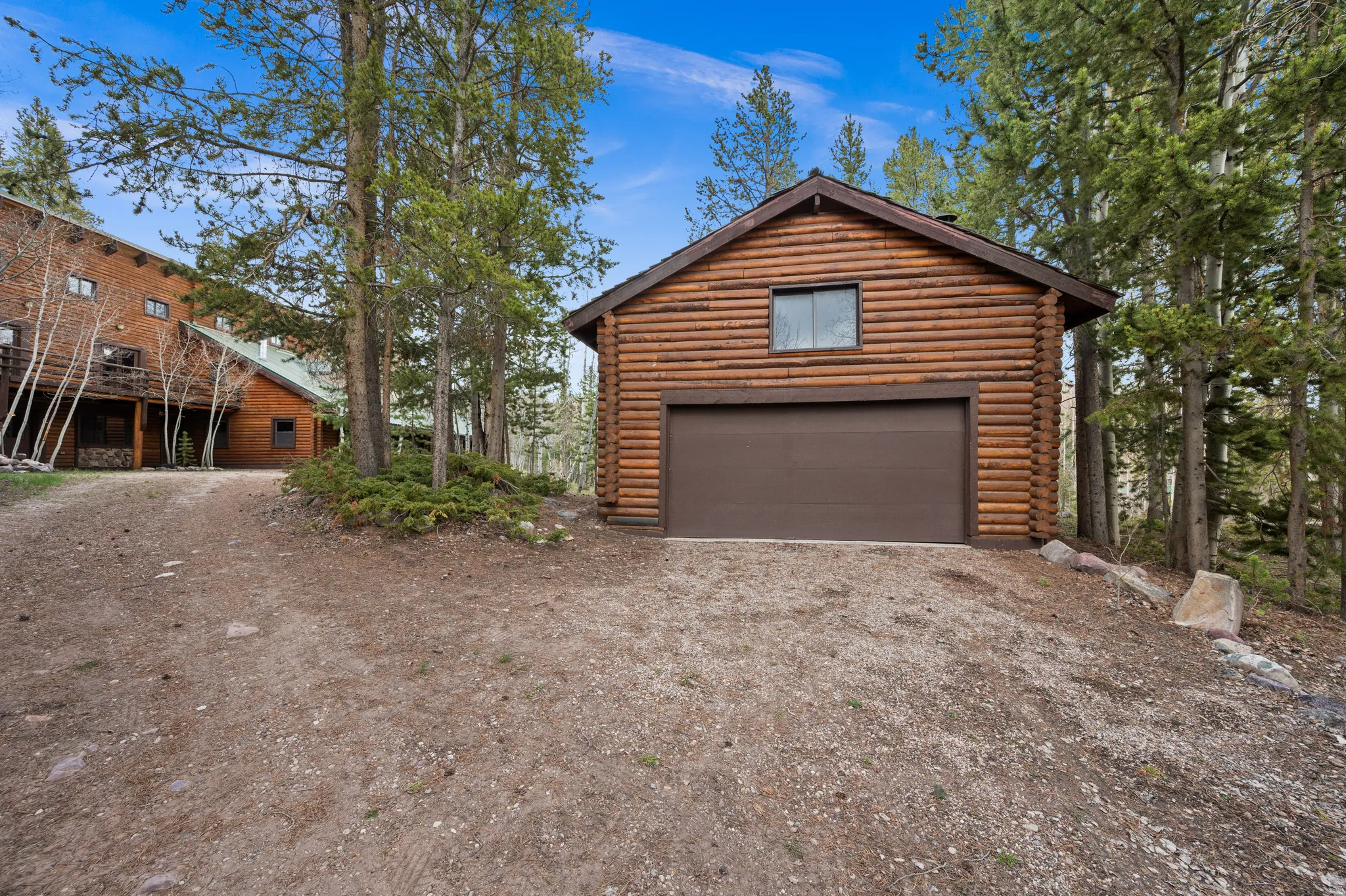 Detached log-style garage featuring a brown overhead door, a single upper window, and a gabled roofline