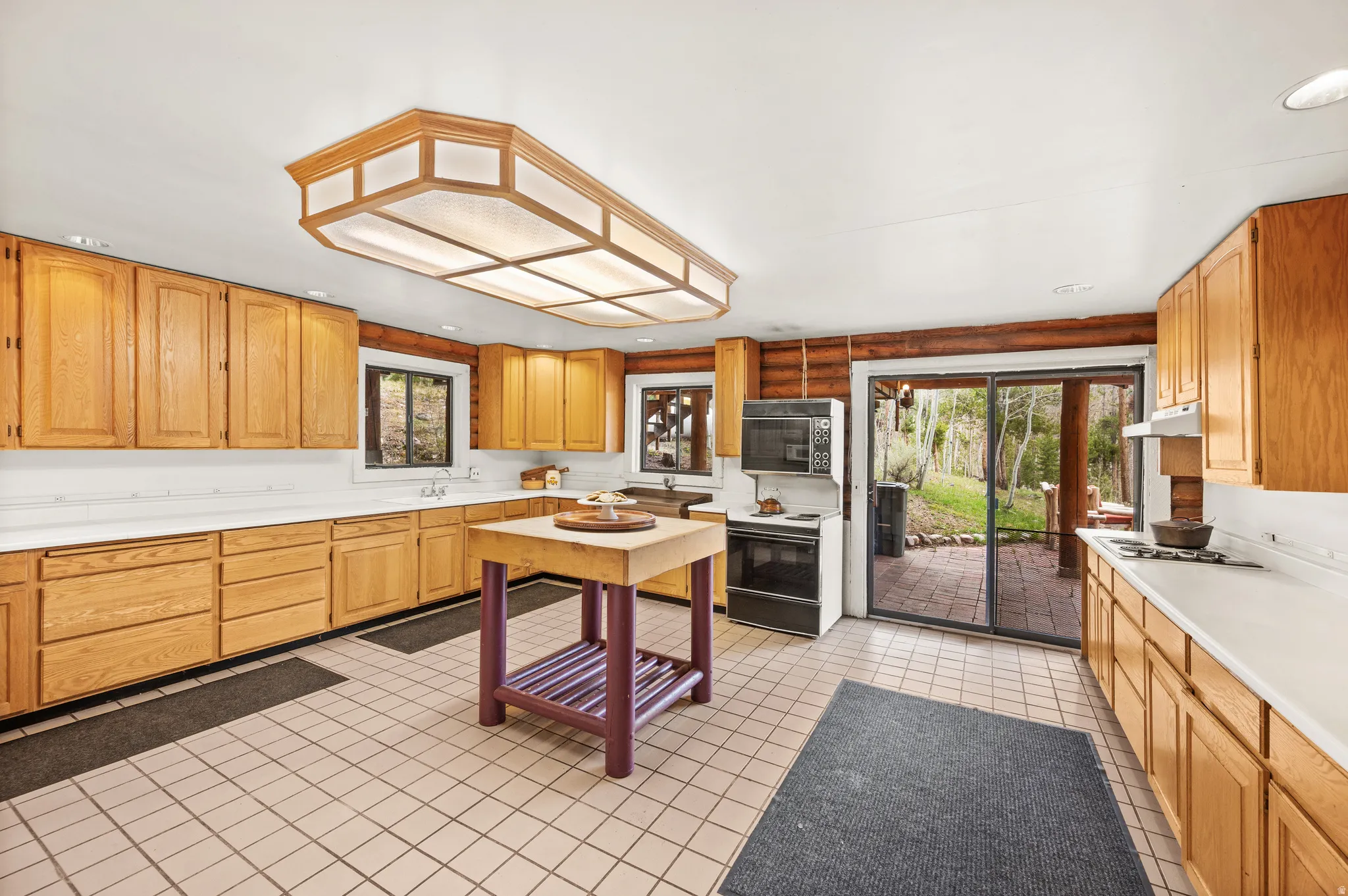 Spacious kitchen featuring light wood cabinetry, white countertops, a central island, and tile flooring