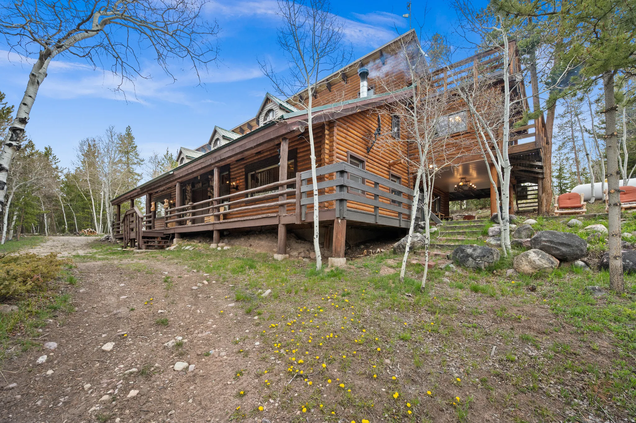 Log cabin exterior with a full-length covered porch, visible dormer windows, and a multi-level deck