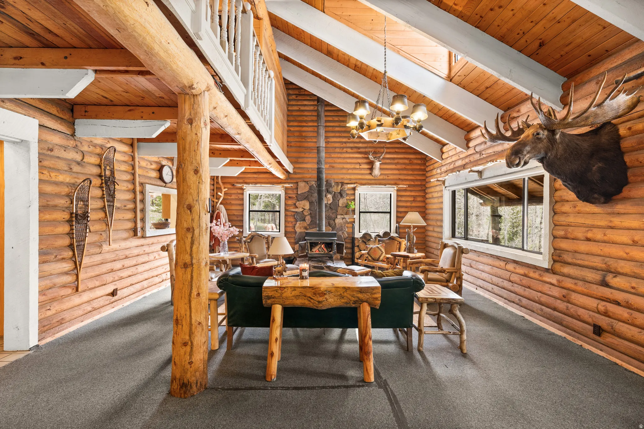 Great room featuring natural wood-finish log walls, a vaulted ceiling with exposed beams, and dark grey carpeting