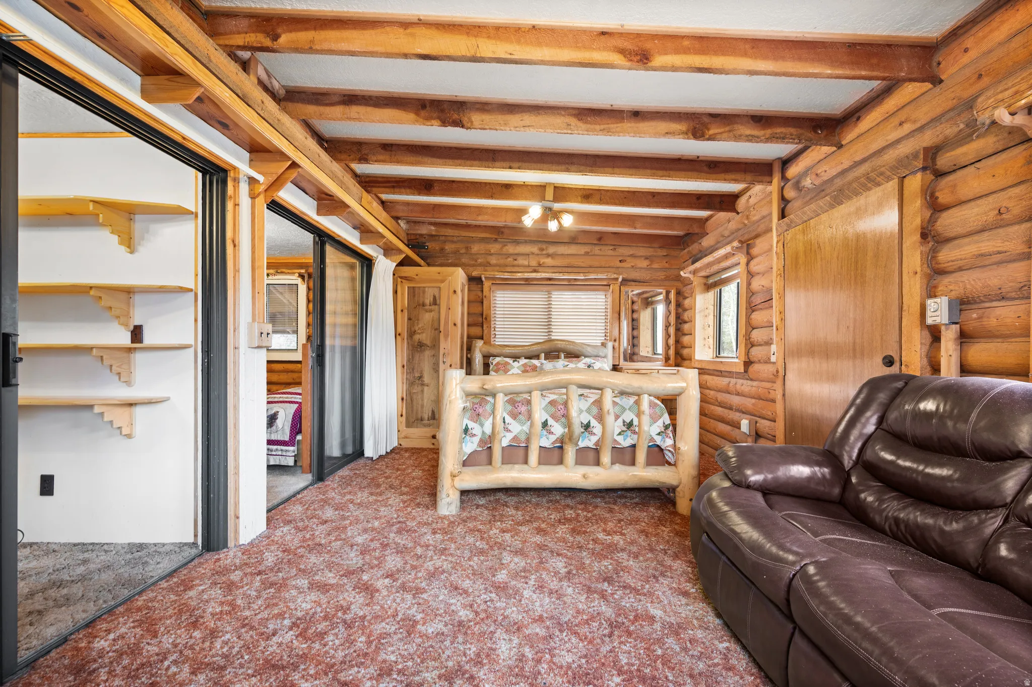 Interior space featuring log walls, exposed wood beams, and a ceiling fan with integrated lighting