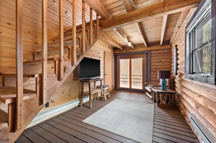 Wood-paneled interior featuring an open staircase with wood railings, exposed wood beam ceiling, and wood-finish flooring