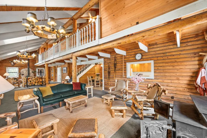 Vaulted wood-paneled ceiling with exposed beams, wood-finish walls, a second-story balcony with white railing, a built-in wood-burning stove, and a visible staircase