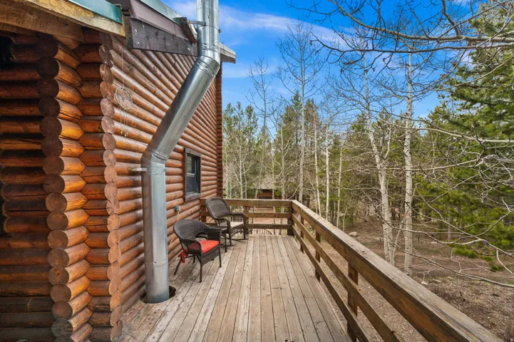 Expansive wood deck with a natural wood railing, featuring a log cabin exterior and mature trees beyond