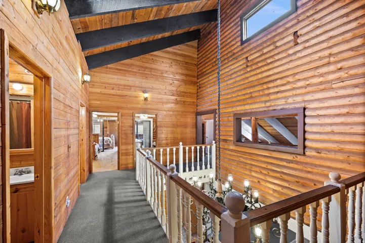 Upper-level hallway featuring extensive wood paneling, exposed wood beams, vaulted ceilings, and a light-colored wood railing