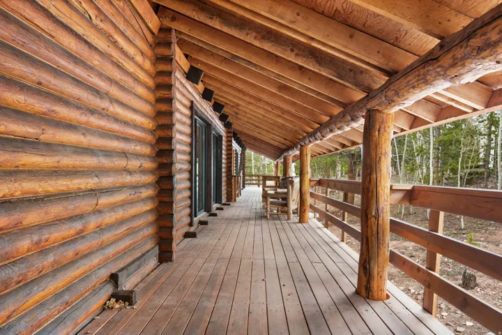 Expansive covered porch featuring a log construction exterior, wood-plank flooring, and a natural wood railing