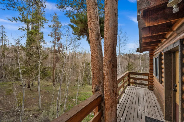 Exterior log cabin architecture featuring a wood deck with wood railings, framed by mature trees, and surrounded by a natural wooded landscape