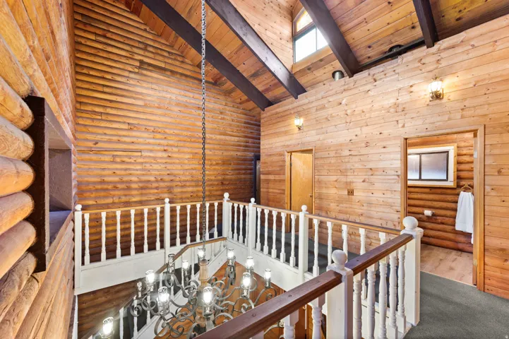 Expansive interior featuring log walls, an open-tread staircase with white balusters, and a vaulted ceiling with exposed wood beams