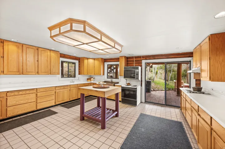 Spacious kitchen featuring light wood cabinetry, white countertops, a central island, and tile flooring