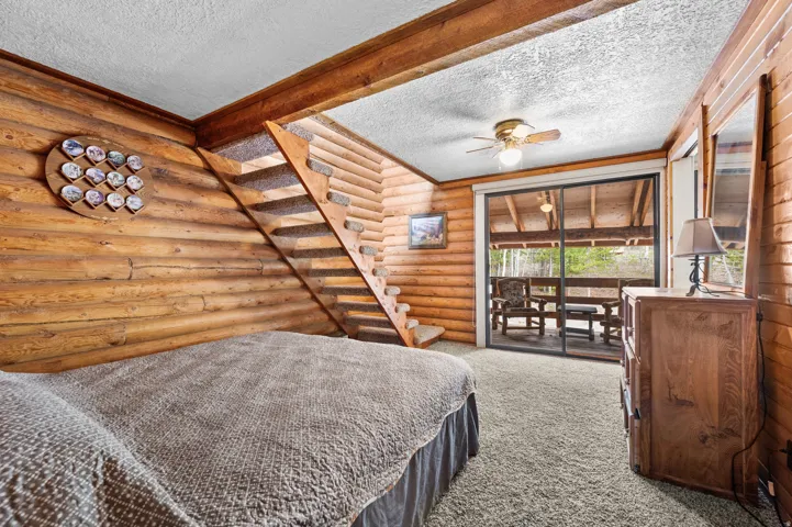Wood-paneled room featuring a staircase with carpeted treads, a ceiling fan with integrated lighting, and a sliding glass door leading to an outdoor deck