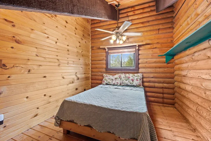 Rustic interior featuring log walls, wood-finish flooring, and a ceiling fan with integrated lighting
