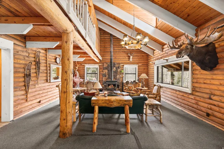 Great room featuring natural wood-finish log walls, a vaulted ceiling with exposed beams, and dark grey carpeting