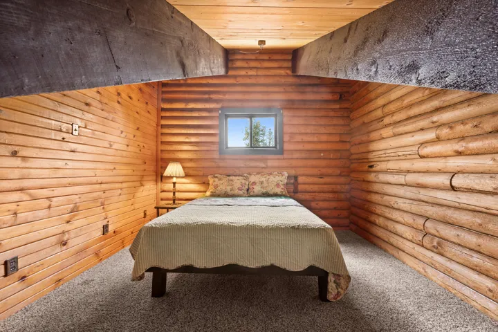 Rustic room with wood-paneled walls, exposed timber beams, and a window providing natural light