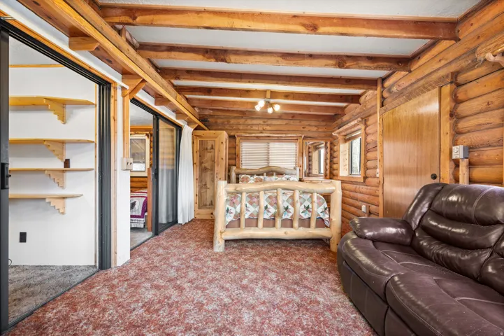 Interior space featuring log walls, exposed wood beams, and a ceiling fan with integrated lighting