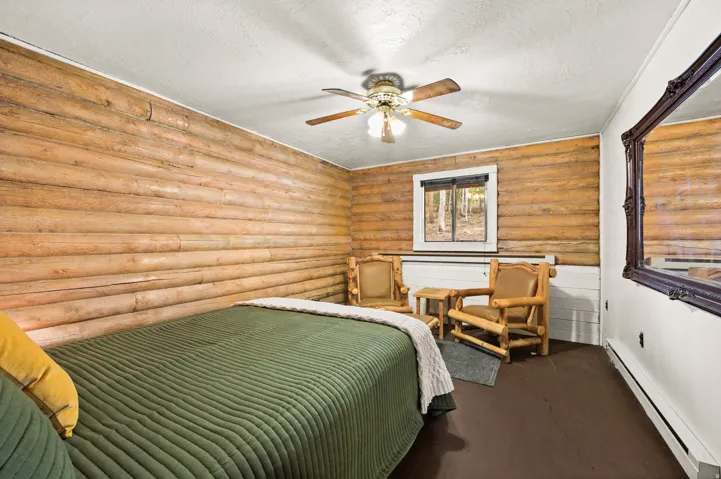 Room with natural wood log walls, a window overlooking trees, and a ceiling fan