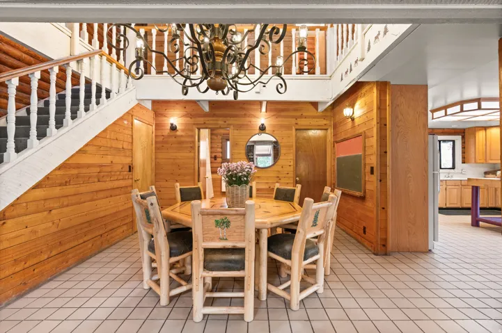 Spacious dining area featuring wood-paneled walls, tile flooring, and a decorative chandelier