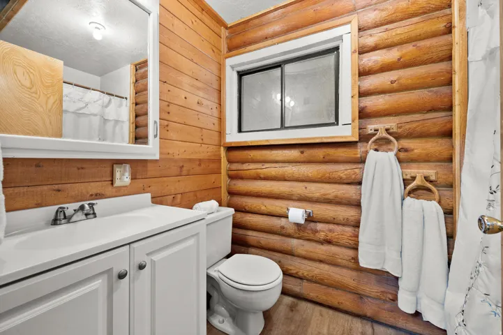 Bathroom featuring log-style wood paneling, a white vanity with an integrated sink, a built-in mirrored medicine cabinet, a toilet, and a window with a wood frame