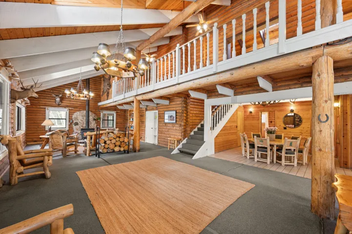 Vaulted ceilings with exposed wood beams, a prominent stone-clad fireplace, and a second-story loft with a white spindle railing
