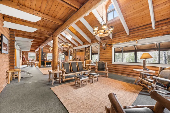 Vaulted wood-paneled ceilings with exposed white beams, log-style wall construction, window with arched transom, full-wall horizontal windows, and gray carpet flooring