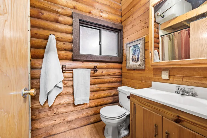 Bathroom featuring natural wood plank and log walls, a white toilet, and a vanity with a white countertop and natural wood cabinetry