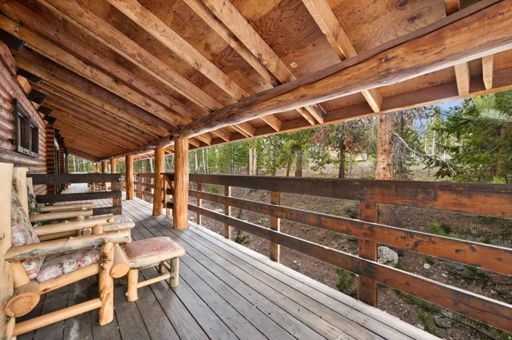 Expansive covered porch featuring wood-finish flooring, log beam construction, and a wooden railing system