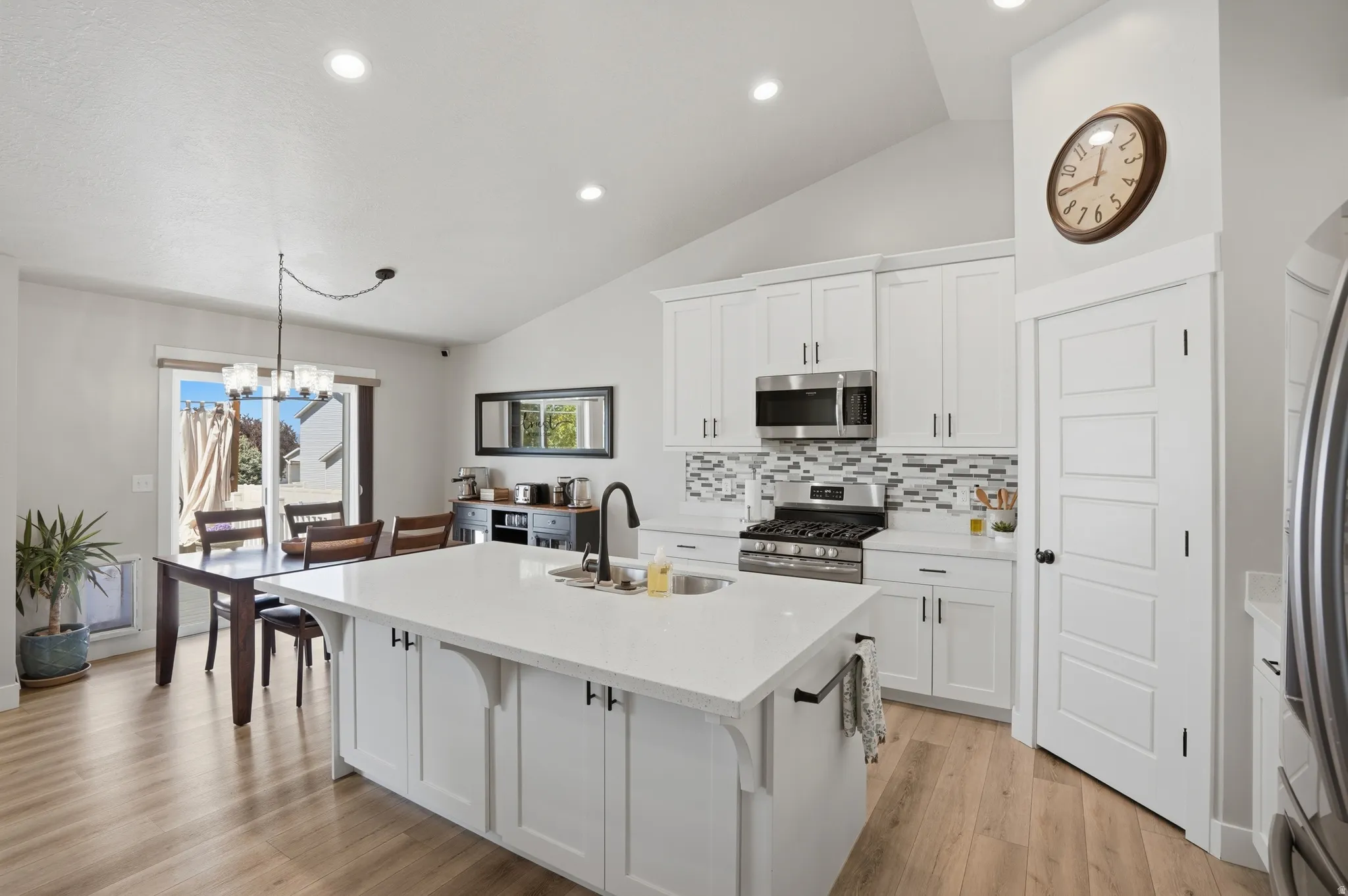 Open-concept kitchen featuring white shaker cabinetry, stainless steel appliances, a center island with a sink, wood-finish flooring, and a dining area with direct outdoor access