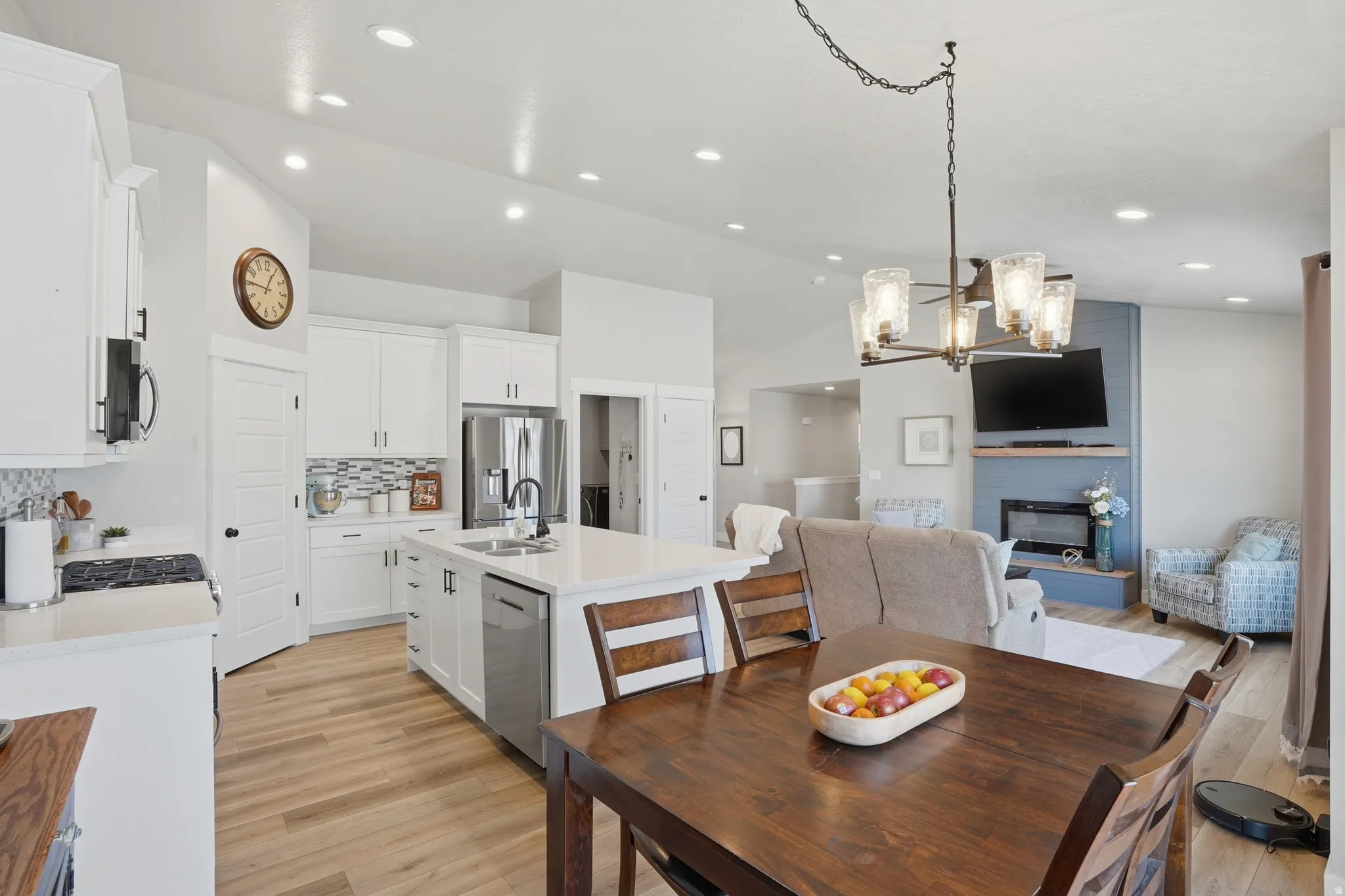 Bright open-concept kitchen and living area featuring white cabinetry, a large kitchen island with counter seating, stainless steel appliances, and wood-finish flooring