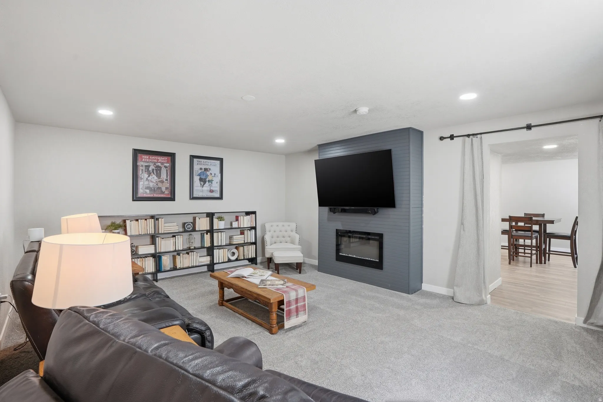 Spacious family area featuring recessed lighting, gray carpeting, a built-in electric fireplace with a gray shiplap surround, and an adjacent open entryway with wood-finish flooring