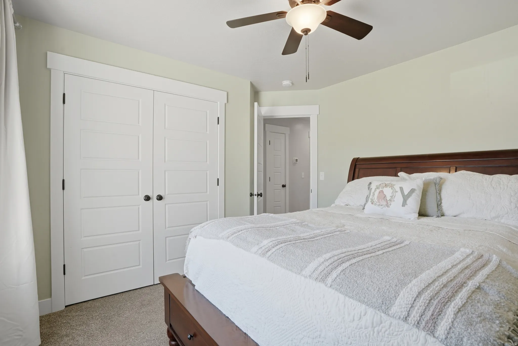 Bedroom featuring soft green walls, wood-finish headboard, textured carpeting, and a ceiling fan with integrated lighting