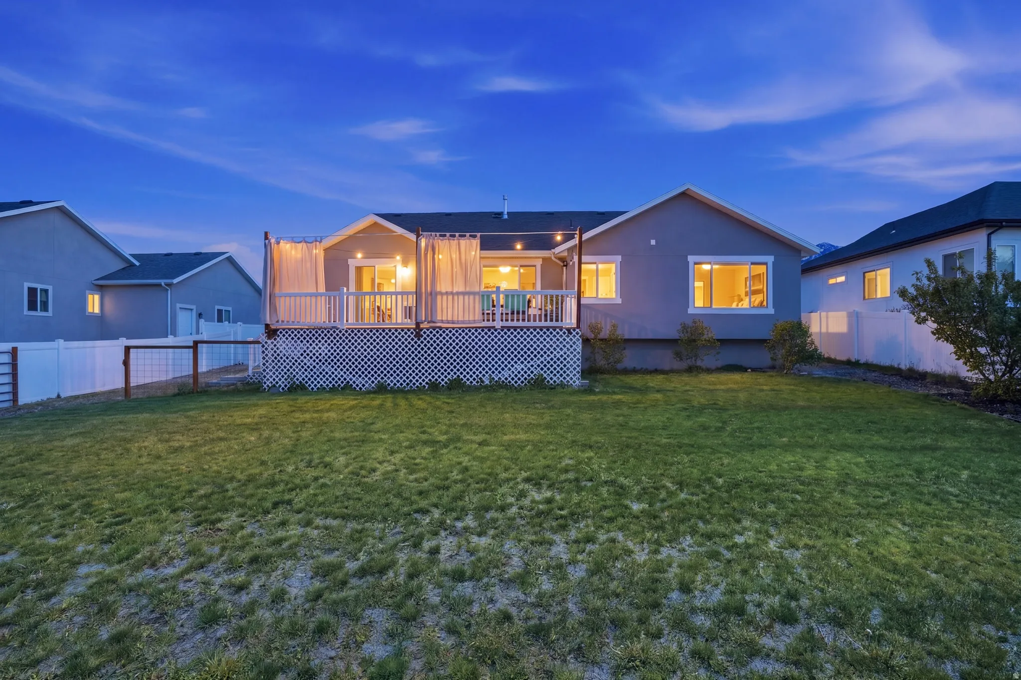 Spacious backyard featuring a manicured lawn, an elevated deck with white lattice skirting, and a white privacy fence