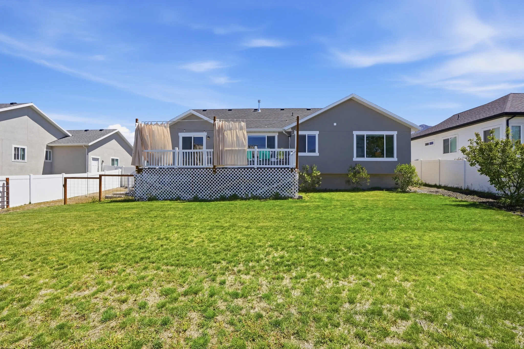 Expansive backyard featuring a green lawn, white vinyl fencing, and a raised composite deck with white railings and lattice skirting