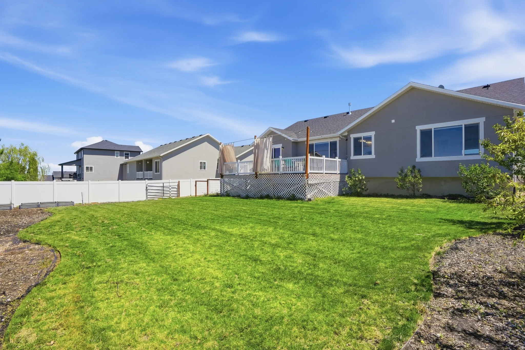 Spacious backyard featuring a manicured lawn, an elevated deck with white lattice skirting, and a white vinyl privacy fence